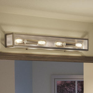 The Urban Ambiance UHP2752 Luxe Industrial Electric Bath Fixture from the Messina Collection, featuring a sleek stainless steel finish and measuring 4-1/2 inches high by 30 inches wide, offers a stylish modern touch when mounted above a doorway on a light-colored wall.