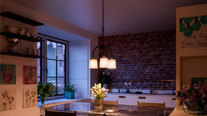 A modern kitchen features an exposed brick wall, a Boise Collection UHP2764 Transitional Chandelier by Urban Ambiance in Olde Bronze finish hanging as a pendant above the table adorned with a vase of tulips, complemented by a large window and vibrant artwork on the walls.
