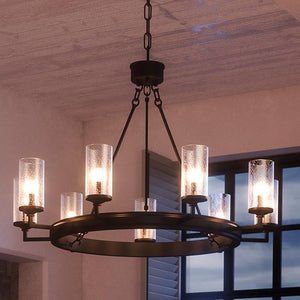 The UHP2892 XL Rustic Chandelier from Urban Ambiance's Livorno Collection features eight seeded glass shades and a charcoal finish, hanging in a room with an open window. Size: 24-7/8