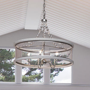 A unique lighting fixture, the Urban Ambiance UHP3410 Provincial Chandelier brings a galvanized steel finish to the Layton Collection, hanging over a window in a living room.