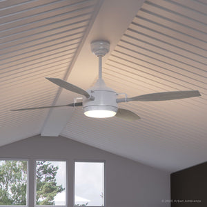 The UHP9012 Urban Loft Ceiling Fan from the Mendocino Collection by Urban Ambiance, featuring four blades and a central light fixture in matte white, is mounted on a white vaulted ceiling above four rectangular windows.