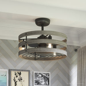 The UHP9031 Modern Farmhouse Indoor Ceiling Fan by Urban Ambiance, from the Adelaide Collection, features a layered wood and metal design in charcoal with exposed bulbs—evoking a rustic industrial style—beautifully installed in a modern room adorned with chevron-patterned wallpaper and framed art.