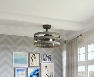 The Urban Ambiance UHP9031 Modern Farmhouse Indoor Ceiling Fan from the Adelaide Collection, featuring metal blades and a charcoal finish, brings rustic industrial style to a bright room with framed art on a herringbone-patterned wall and large windows dressed with light curtains.