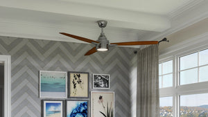 An Urban Ambiance UHP9041 Mid Century Modern Indoor Ceiling Fan from the Tybee Collection, featuring wooden blades, a central light fixture, and a brushed nickel finish (13.1″H x 60″W), is installed in a room with large windows dressed in gray curtains, herringbone-patterned walls, and picture frames.