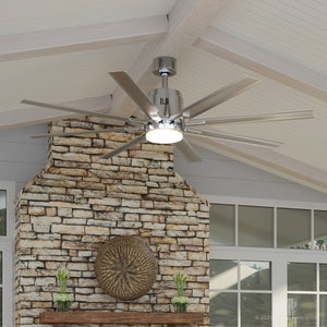 A UHP9051 Urban Loft Indoor / Outdoor Ceiling Fan from the Chatham Collection by Urban Ambiance, featuring a brushed nickel finish, eight blades, and an integrated LED light (16.8″H x 72″W), is mounted above a stone fireplace in a room with a white vaulted ceiling.