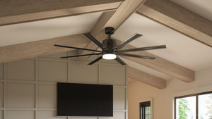 A spacious modern room with natural lighting and a wall-mounted TV features the Urban Ambiance UHP9053 Urban Loft Indoor / Outdoor Ceiling Fan from the Chatham Collection, measuring 72 inches wide by 16.8 inches high in an Olde Bronze finish, elegantly mounted on a wooden-beamed ceiling and equipped with a dimmable LED light.