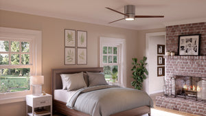 A bedroom featuring a neatly made bed, windows, a nightstand, framed art, a potted plant, and a brick fireplace with a lit fire is illuminated by the Urban Ambiance UHP9070 Modern Indoor Ceiling Fan from the Camden Collection in brushed nickel (9.9″H x 56″W), which includes an integrated LED light.