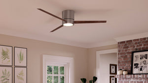 The Urban Ambiance UHP9070 Modern Indoor Ceiling Fan from the Camden Collection, featuring three wooden blades and an integrated LED light in a brushed nickel finish (9.9″H x 56″W), is installed on a white ceiling in a living room adorned with framed art and a brick fireplace.