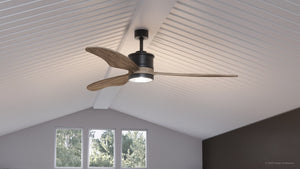 The UHP9090 Modern Indoor Ceiling Fan from Urban Ambiance’s Lewes Collection, featuring solid wood blades, a built-in LED light, and a sleek charcoal finish, is mounted on a white vaulted ceiling above the windows.