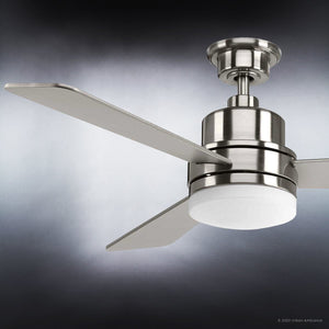 The Urban Ambiance UHP9210 Modern Indoor Ceiling Fan from the Capitola Collection features three metallic blades and an integrated light fixture, finished in brushed nickel and mounted on a metal rod, set against a gray gradient background.