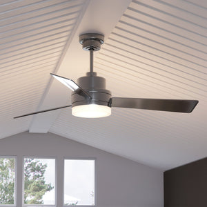 The Urban Ambiance UHP9210 Modern Indoor Ceiling Fan from the Capitola Collection, featuring a brushed nickel finish, three sleek blades, and a built-in light fixture (15.8″H x 52″W), is mounted on a white sloped ceiling in a room with large windows.
