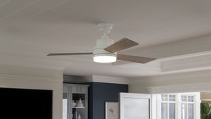 The UHP9212 Modern Indoor Ceiling Fan from the Capitola Collection by Urban Ambiance, featuring three wooden blades and an integrated LED light, is mounted on a white paneled ceiling in a bright, contemporary room. Measuring 15.8 inches high by 52 inches wide, this energy-saving fan seamlessly blends stylish design with exceptional functionality.