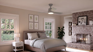 Bedroom featuring a bed, nightstand, lamp, brick fireplace, framed pictures, windows with an outside view, and the UHP9221 Modern Indoor Ceiling Fan (15.6″H x 44″W) in Brushed Nickel from the Capitola Collection by Urban Ambiance.