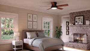 A bedroom featuring a bed, nightstand, lamp, and the UHP9230 Traditional Indoor Ceiling Fan from the Beaufort Collection by Urban Ambiance in Olde Bronze with American Walnut blades; additional elements include a fireplace, framed art on the walls, and windows overlooking lush greenery outside.