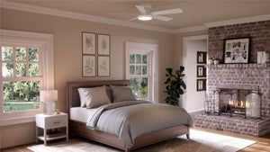 Bedroom featuring a gray bed, wooden nightstand, illuminated fireplace, brick accent wall, framed art, and windows overlooking lush greenery. The space is elevated by an Urban Ambiance UHP9232 Traditional Indoor Ceiling Fan from the Beaufort Collection—measuring 11.6″H x 52″W in white—with an integrated LED light and opal glass diffuser on the ceiling.
