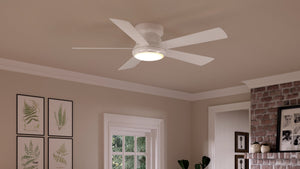 A white Urban Ambiance UHP9232 Traditional Indoor Ceiling Fan from the Beaufort Collection, featuring an integrated LED light and an opal glass diffuser, is installed on a beige ceiling in a room with framed plant prints, a window, and part of a brick wall visible.