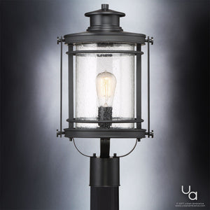 The Urban Ambiance UQL1010 Mid-Century Modern Outdoor Post Light from the Cannes Collection features a black silk finish with a sleek metallic frame, a clear seeded glass cylindrical shade showcasing the visible bulb inside—all elegantly displayed against a gray gradient backdrop.