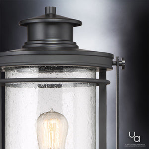 Close-up of the Urban Ambiance UQL1010 Mid-Century Modern Outdoor Post Light from the Cannes Collection, featuring a black silk finish and seeded glass shade showcasing a visible bulb, beautifully illuminated against a dark background.