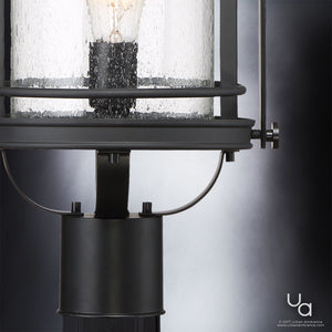 Close-up of the UQL1010 Mid-Century Modern Outdoor Post Light from the Cannes Collection by Urban Ambiance, featuring a glass enclosure, visible bulb, and black silk metal frame set against a gradient gray background; measures 19.5″H x 10.5″W.