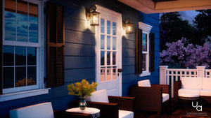 At dusk, a blue house’s porch is lit by Urban Ambiance Vienna Collection UQL1040 Craftsman Outdoor Wall Lights in natural black, with seeded glass flanking the white door, creating timeless style alongside wicker chairs and flowers.
