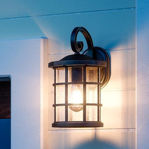 The Urban Ambiance UQL1041 Craftsman Outdoor Wall Light, 11"H x 6"W, Oil Rubbed Parisian Bronze, Vienna Collection, is mounted on a light exterior wall and shines beautifully at dusk with its clear seeded glass shade.