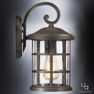 The UQL1043 Craftsman Outdoor Wall Light by Urban Ambiance features a marine-grade metal frame in a Parisian Bronze finish, with a cylindrical seedy glass enclosure and visible illuminated bulb, measuring 14.25″ high by 8″ wide from the Vienna Collection.