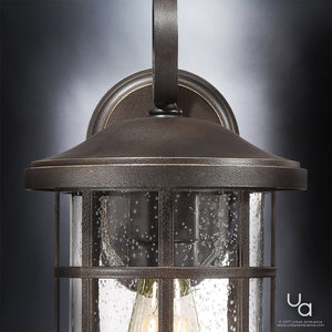 Close-up of the Urban Ambiance UQL1043 Craftsman Outdoor Wall Light from the Vienna Collection, featuring a Parisian Bronze finish, a gracefully curved top, and clear seedy glass panels that display an elegant water droplet texture. This 14.25″ tall by 8″ wide outdoor sconce also boasts marine-grade construction for lasting durability.