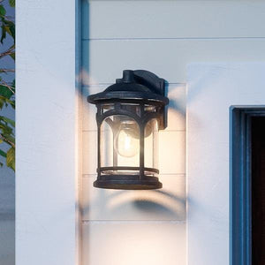 The Urban Ambiance UQL1100 Rustic Outdoor Wall Light, featuring a black silk finish and clear seeded glass, is mounted beside the doorway to illuminate the exterior.