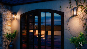 Double glass doors with black frames open to a well-lit interior dining area; on either side of the entrance, weather-resistant Urban Ambiance UQL1101 Rustic Outdoor Wall Lights from the Sydney Collection, featuring an 11-inch by 7-inch marine-grade Parisian Bronze finish and seeded glass, illuminate the space alongside potted plants.
