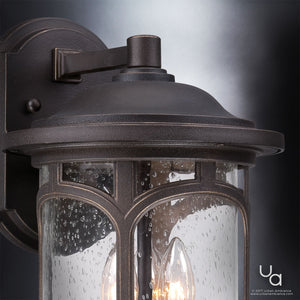 Here’s a revised version of the sentence using your product data: Close-up of the Urban Ambiance UQL1103 Rustic Outdoor Wall Light from the Sydney Collection, featuring a Parisian Bronze finish and marine-grade construction; its 14.5″ x 9″ form displays a clear seeded glass shade with raindrop texture and a visible candle-style bulb, elegantly mounted on an exterior wall.
