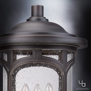 Close-up of the UQL1107 Rustic Outdoor Post Light from the Sydney Collection by Urban Ambiance, shown in a Parisian Bronze finish with clear seeded glass panels that highlight its raindrop-like details. This elegant outdoor lantern measures 19″ high by 11″ wide and features marine-grade construction, with the Urban Ambiance logo visible in the bottom right corner.