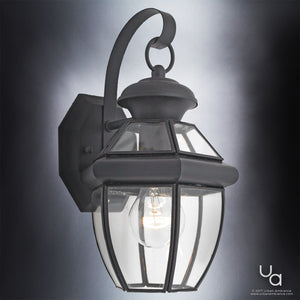 The Urban Ambiance UQL1140 Colonial Outdoor Wall Light from the Cambridge Collection features a black silk finish, clear glass panels, and an exposed bulb within a sturdy metal frame. Measuring 11.5 inches high by 7 inches wide, this elegant wall-mounted fixture showcases timeless colonial design with modern sophistication, as photographed against a neutral background.