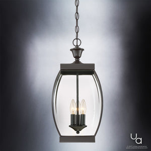 The Urban Ambiance UQL1176 Colonial Outdoor Pendant Light from the Manchester Collection features a medieval bronze finish and measures 20.5 inches high by 9 inches wide; it showcases three exposed candle-style bulbs within beveled glass panels, suspended by a chain against a gray gradient background.