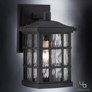 The UQL1230 Craftsman Outdoor Wall Light by Urban Ambiance features a black silk finish, clear textured glass, a visible bulb, and subtle cage accents. Measuring 10.5