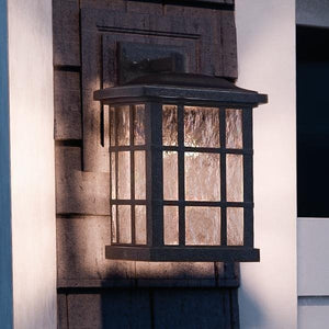 The Urban Ambiance UQL1235 Craftsman Outdoor Wall Light from the Zurich Collection features a Parisian Bronze finish and marine-grade construction. Measuring 15.5 inches high by 9.5 inches wide, this black metal outdoor wall lantern with glass pane detailing is mounted on the exterior wall of a building. Designed to be weather-resistant, it serves as an elegant and durable outdoor wall sconce—perfect for enhancing any exterior space.