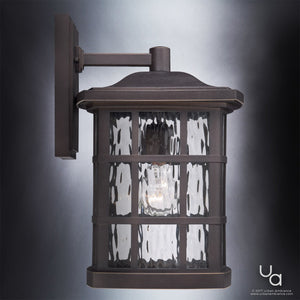 The UQL1235 Craftsman Outdoor Wall Light from Urban Ambiance’s Zurich Collection features a 15.5″ x 9.5″ wall-mounted design with a Parisian Bronze finish, marine-grade construction for weather resistance, and clear textured glass panels that showcase a visible bulb inside.