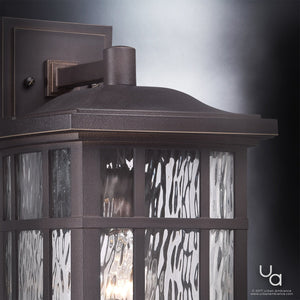 Close-up of the Urban Ambiance UQL1235 Craftsman Outdoor Wall Light from the Zurich Collection, featuring a marine-grade, weather-resistant Parisian Bronze finish and textured glass panels. Its sturdy 15.5″H x 9.5″W dark metal frame is beautifully illuminated from within.