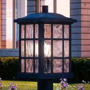 A luxury lighting fixture, an UQL1246 Craftsman Outdoor Post Light from the Zurich Collection by Urban Ambiance, with a black silk finish and glass shade in front of a house.
