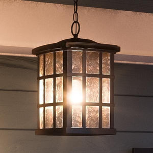 The Urban Ambiance UQL1251 Craftsman Outdoor Pendant Light from the Zurich Collection features a durable marine-grade metal frame in a Parisian Bronze finish, measuring 15″ high by 9.5″ wide. This hanging pendant includes glass panels with an illuminated water glass diffuser and is suspended indoors by a chain, combining both style and function.
