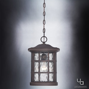 The Urban Ambiance UQL1251 Craftsman Outdoor Pendant Light from the Zurich Collection features a cylindrical frame with clear textured glass panels and a marine-grade Parisian Bronze finish, suspended by a chain and elegantly illuminated against a gradient gray background. The pendant measures 15 inches high by 9.5 inches wide.