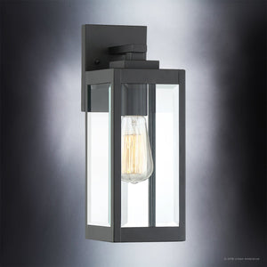 The Urban Ambiance UQL1330 Farmhouse Outdoor Wall Light from the Quincy Collection features a modern black metal frame and beveled glass, showcasing a visible Edison-style bulb that casts a soft glow when mounted on your wall. Expertly blending industrial charm with sleek elegance, this 14.25″ high by 5″ wide fixture is the ideal choice for those seeking a modern farmhouse wall sconce.