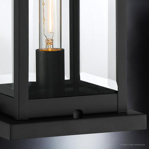 Close-up of the UQL1336 Modern Farmhouse Outdoor Pier Light from the Quincy Collection by Urban Ambiance, featuring a natural black steel finish and clear glass panels that reveal an exposed bulb inside. This 16-inch tall, 7.5-inch wide fixture combines sleek design with functional style, making it an ideal choice for any exterior space.