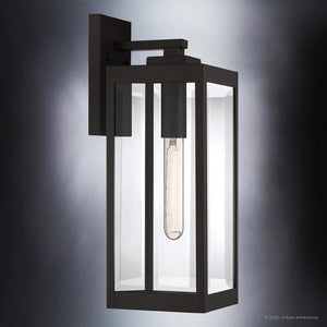 Illuminate your exterior with the UQL1351 Modern Farmhouse Outdoor Wall Light from Urban Ambiance’s Quincy Collection. This rectangular fixture, measuring 17″ high by 6″ wide, features clear glass panels, an exposed vertical filament bulb, and is mounted on a dark backplate. Finished in a rich Estate Bronze, this wall sconce delivers timeless style and welcoming illumination with an elevated modern farmhouse touch.