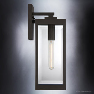 The UQL1351 Modern Farmhouse Outdoor Wall Light by Urban Ambiance features a rectangular black metal frame with clear glass sides and an exposed tubular bulb at its center, all mounted on a flat wall bracket. Measuring 17″ high by 6″ wide and finished in Estate Bronze, this sconce from the Quincy Collection is perfect for adding modern farmhouse lighting to your exterior space, combining style and outdoor durability.