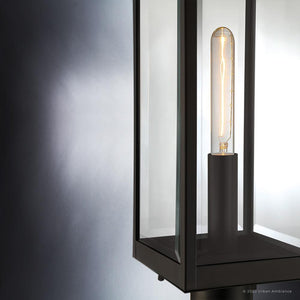 Close-up of the Urban Ambiance UQL1353 Modern Farmhouse Outdoor Post/Pier Light from the Quincy Collection, featuring an estate bronze finish and beveled glass panels. This 20.5-inch tall by 7-inch wide fixture showcases a contemporary black metal frame and exposed tubular bulb, blending modern style with timeless farmhouse appeal against a gray gradient background.