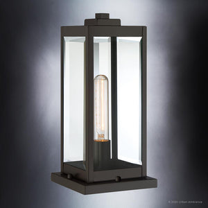 The Urban Ambiance UQL1355 Modern Farmhouse Outdoor Pier Light from the Quincy Collection features a rectangular black metal and glass lantern-style design with an exposed vertical bulb. Measuring 16″ high by 7.5″ wide, it showcases beveled glass panels and a refined Estate Bronze finish, making it an elegant accent for any outdoor setting. Displayed here against a gradient gray background.