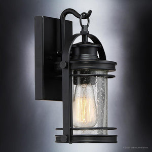 The UQL1430 Nautical Outdoor Wall Light from Urban Ambiance’s Cannes Collection features a Black Silk finish and measures 11.5 inches high by 6.75 inches wide. Showcasing a vintage-inspired design, this outdoor sconce is crafted with clear seeded glass and a rectangular backplate, creating a welcoming ambiance while offering the perfect blend of classic charm and modern durability for any exterior space.