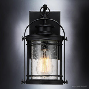 The Urban Ambiance UQL1430 Nautical Outdoor Wall Light from the Cannes Collection features a Black Silk finish and measures 11.5 inches high by 6.75 inches wide. Its clear seedy glass cover, with a unique water droplet texture, houses an exposed filament bulb to create a vintage-inspired lantern look when mounted against any exterior wall.