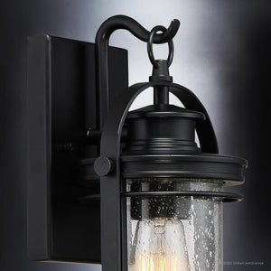 Close-up of the Urban Ambiance UQL1430 Nautical Outdoor Wall Light from the Cannes Collection, measuring 11.5 inches high by 6.75 inches wide, with a Black Silk aluminum finish and a clear seedy glass shade featuring water droplet texture and an exposed bulb inside.