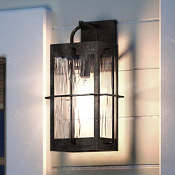 An UQL1464 Ultilitarian Outdoor Wall Light, 14.25"H x 6.25"W, Urban Bronze Finish, Parma Collection hanging on a wall next to a door is